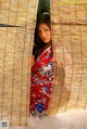 A woman in a red kimono standing in front of a bamboo wall.