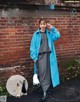 A woman standing in front of a brick wall wearing a blue coat.