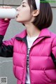 A woman in a pink jacket drinking from a bottle.